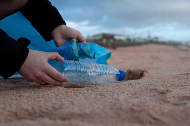 Picture of someone picking up a plastic bottle on a beach.